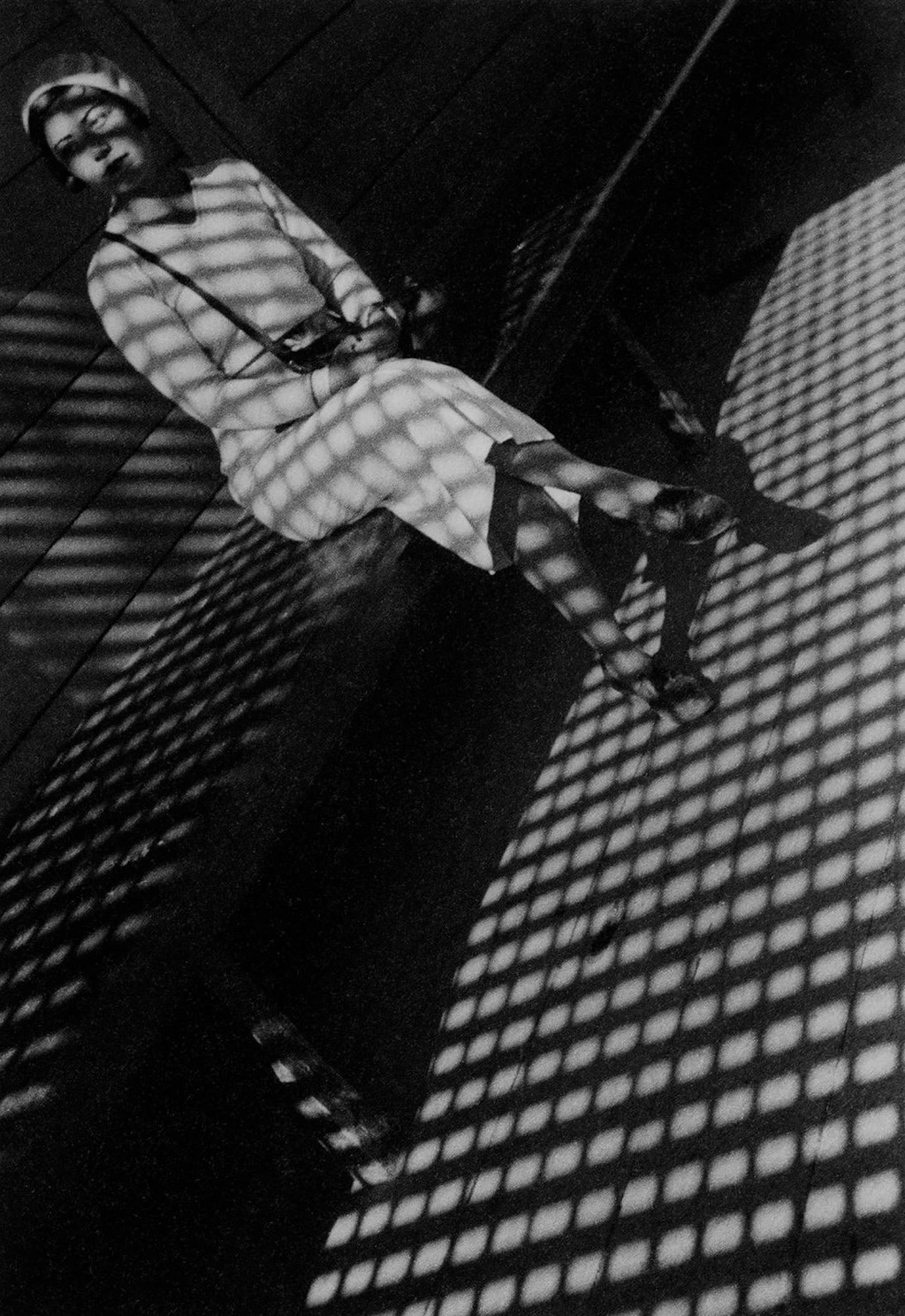 Imagen en blanco y negro, mujer sentada en un banco, juego geométrico de luces y sombras en la estancia